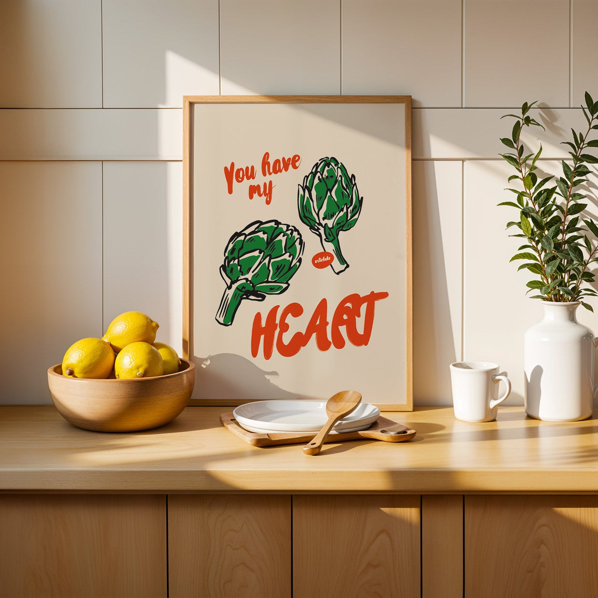 Artichoke print in a slim oak frame leaning on a counter beside a bowl of lemons