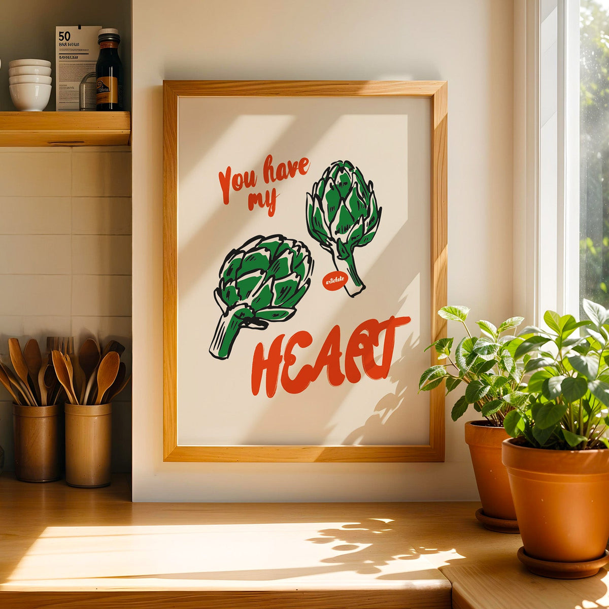 Artichoke print in a light pine frame beside a ceramic jar of wooden spoons