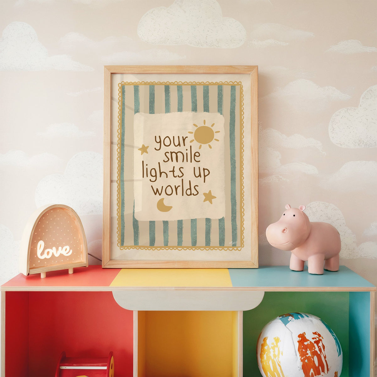 Your smile lights up worlds nursery print in an oak frame on a rainbow toy shelf against cloud wallpaper