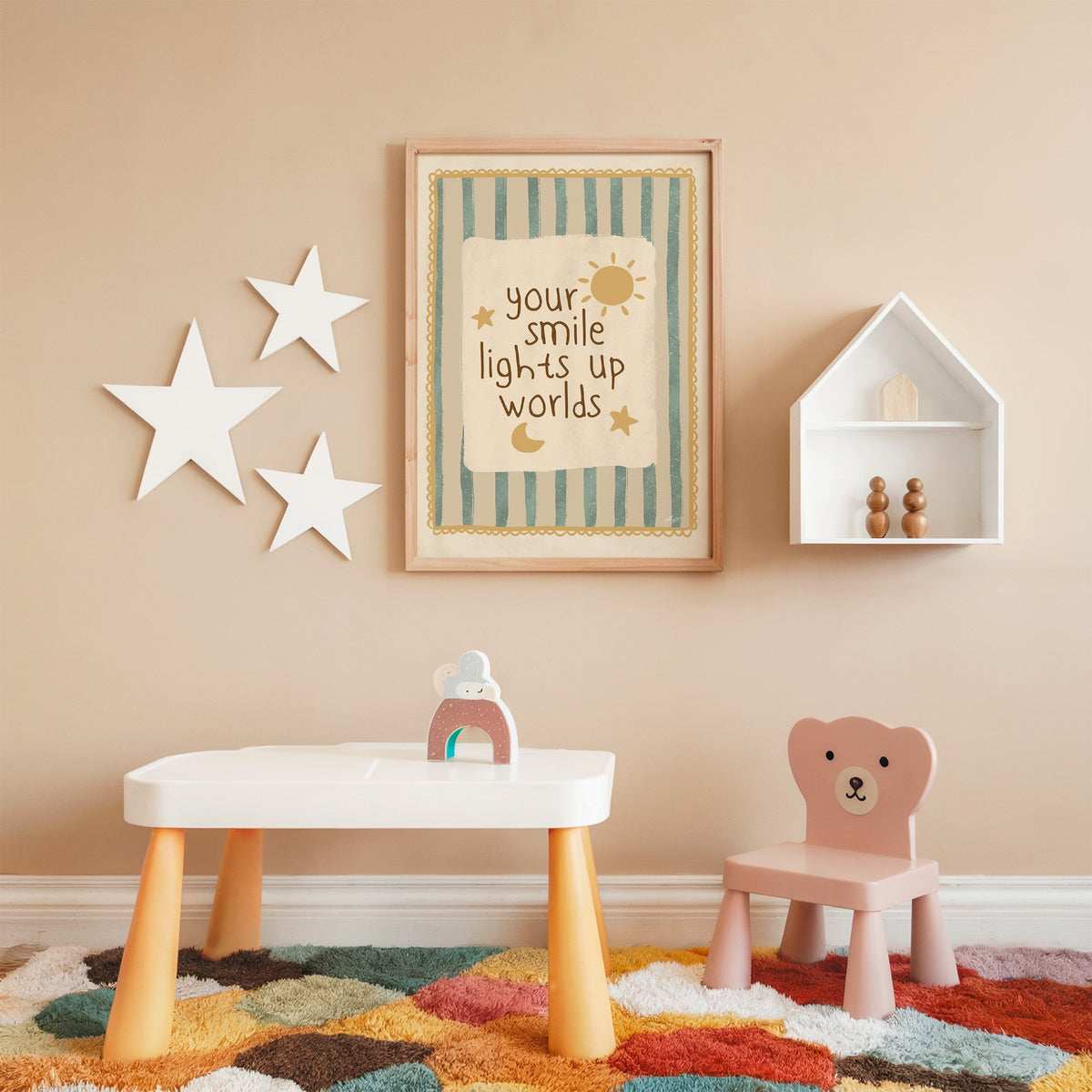Your smile lights up worlds nursery print in an oak frame on a peach wall above a kids table with wall stars