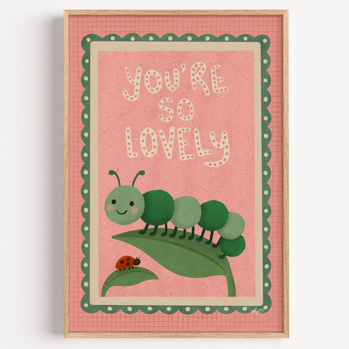 Smiling caterpillar on a leaf nursery print in a light oak frame on a plain white wall