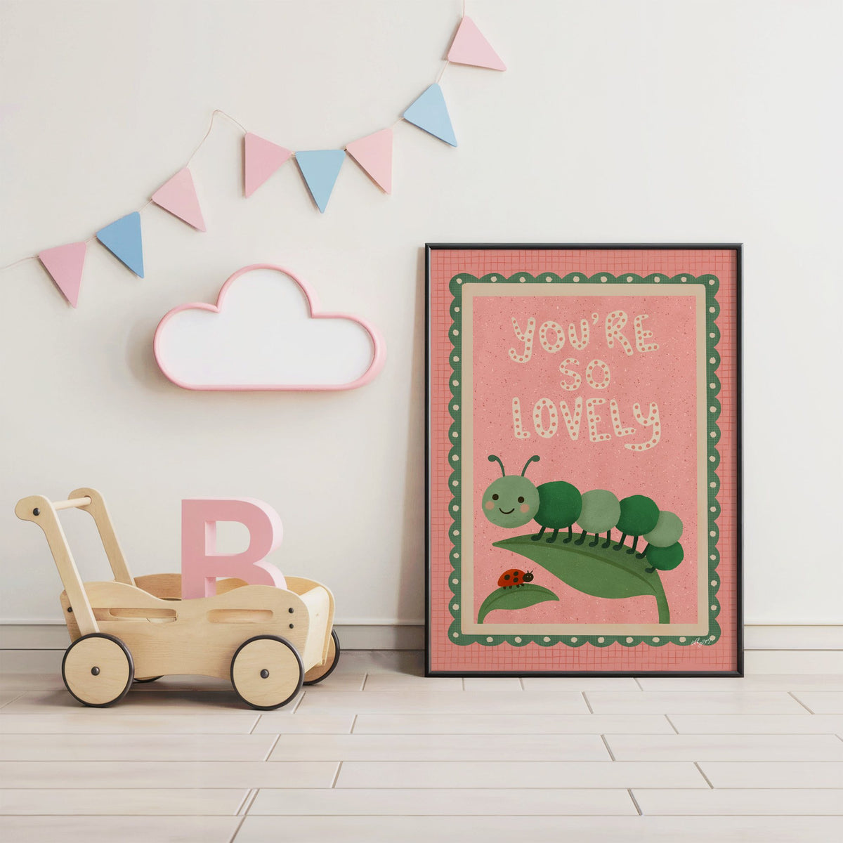 Smiling caterpillar on a leaf nursery print in a black frame under pastel bunting by a wooden baby walker
