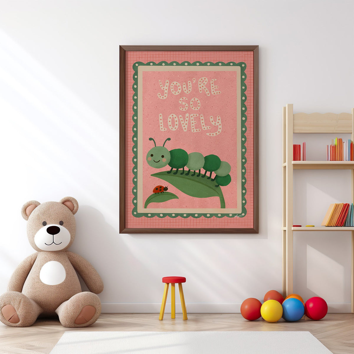 Smiling caterpillar on a leaf nursery print in a walnut frame above a big teddy bear by a bookshelf