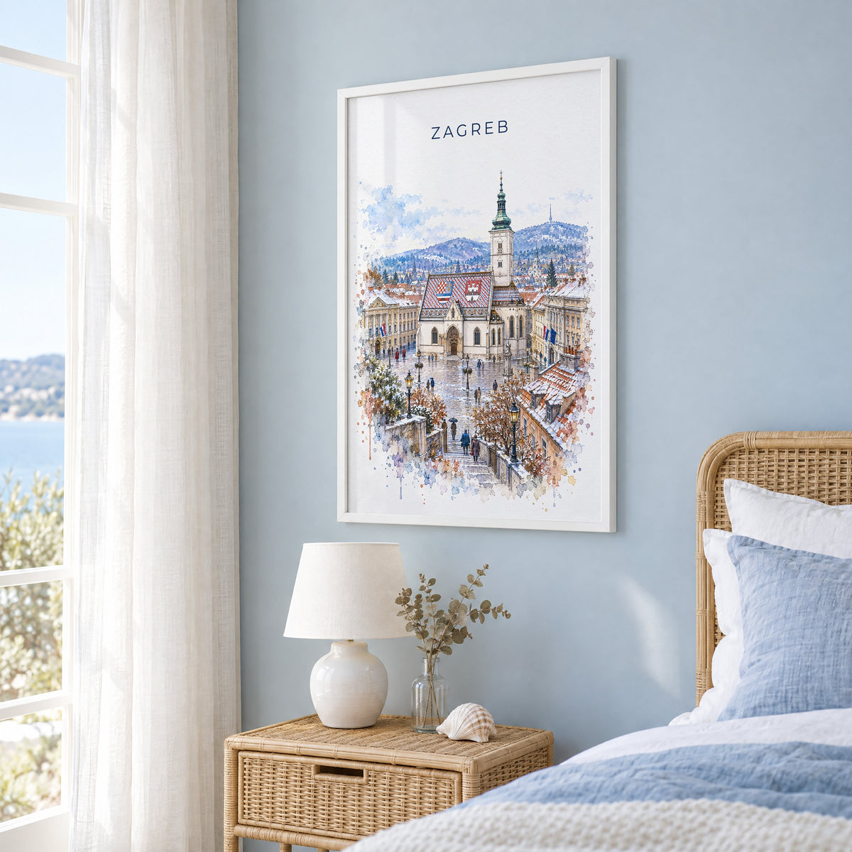 Zagreb watercolor print in a white frame on a pale blue wall beside a rattan bed in a coastal bedroom