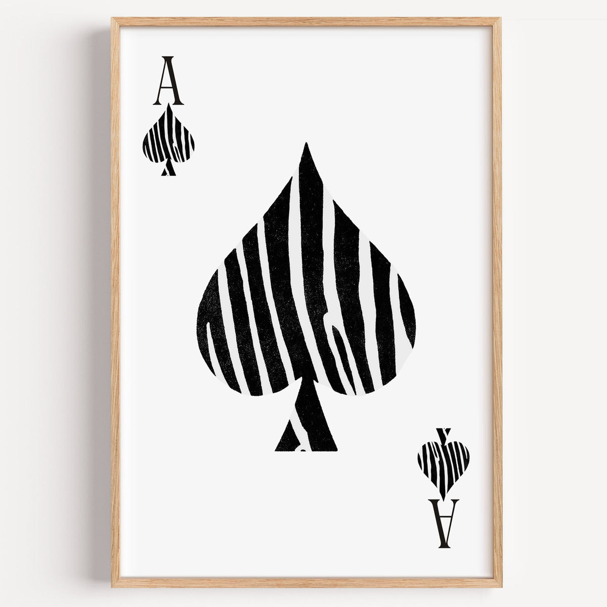 Zebra stripe ace of spades playing card print in a light oak frame on a plain white wall