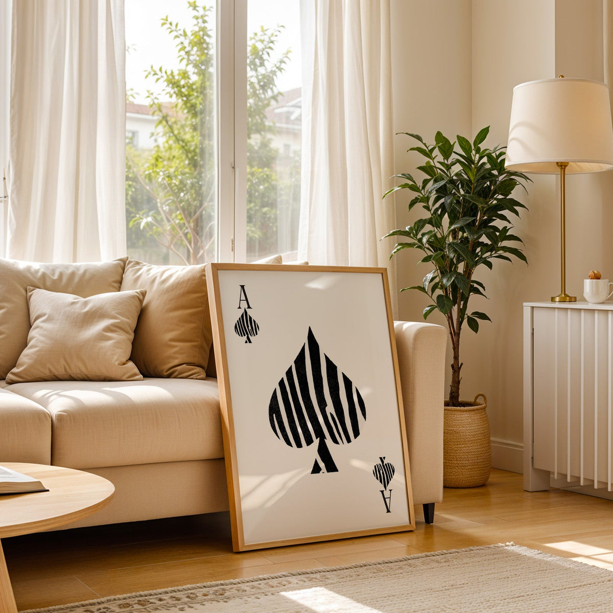 Zebra stripe ace of spades playing card print in a light oak frame leaning on a cream sofa beside a floor lamp