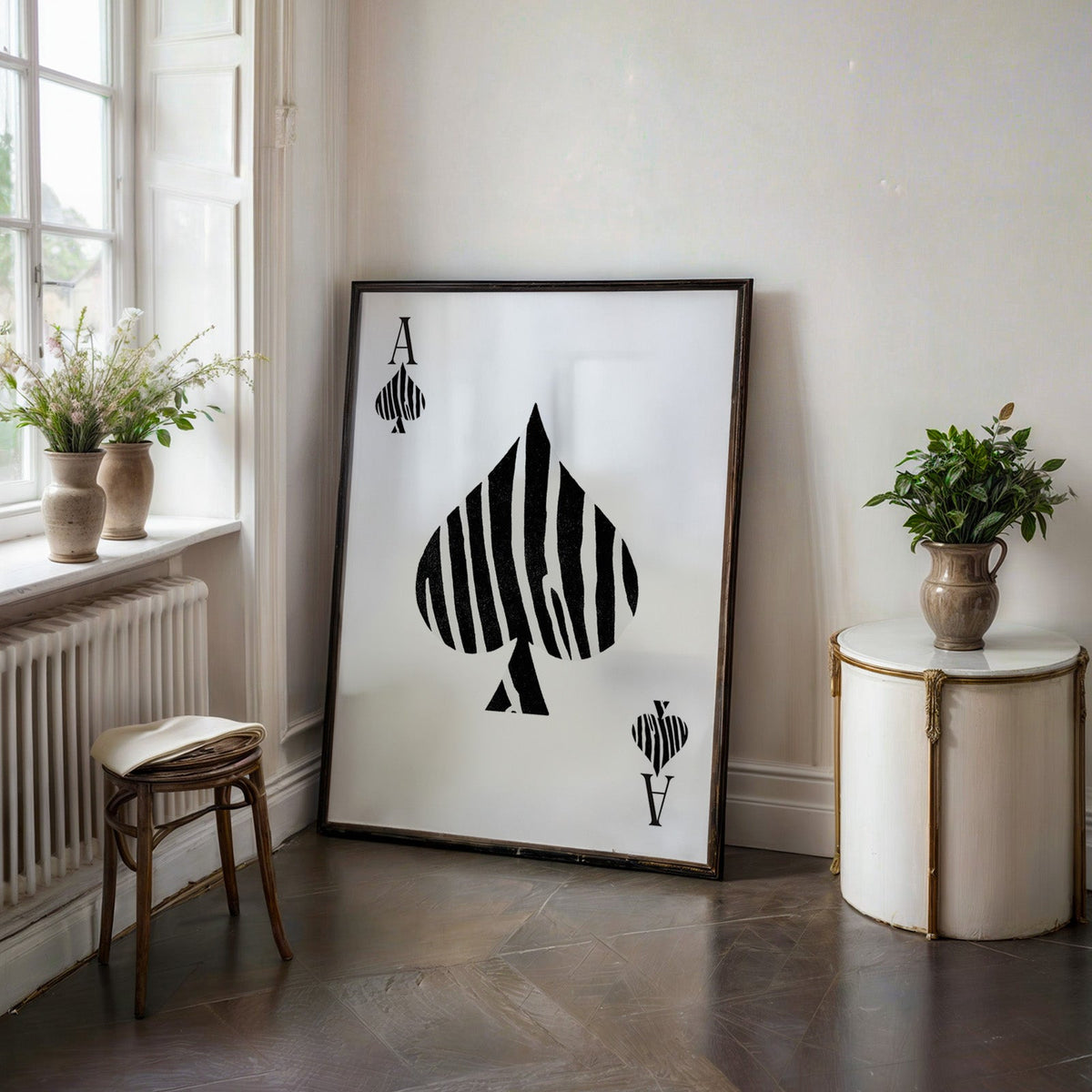 Zebra stripe ace of spades playing card print in a black frame on a dark stone floor beside a white side table