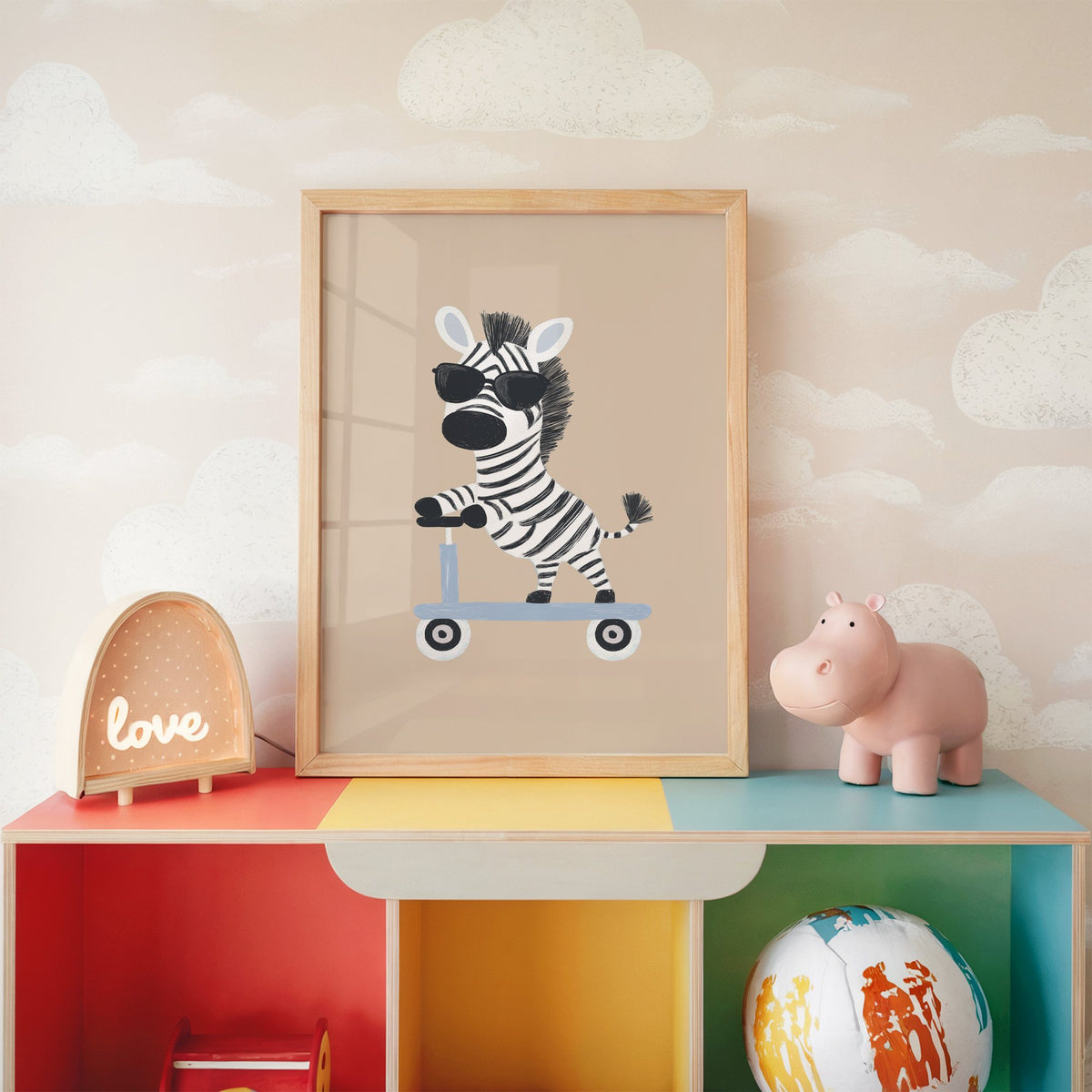 Zebra in sunglasses on scooter nursery print in an oak frame on a rainbow toy shelf against cloud wallpaper
