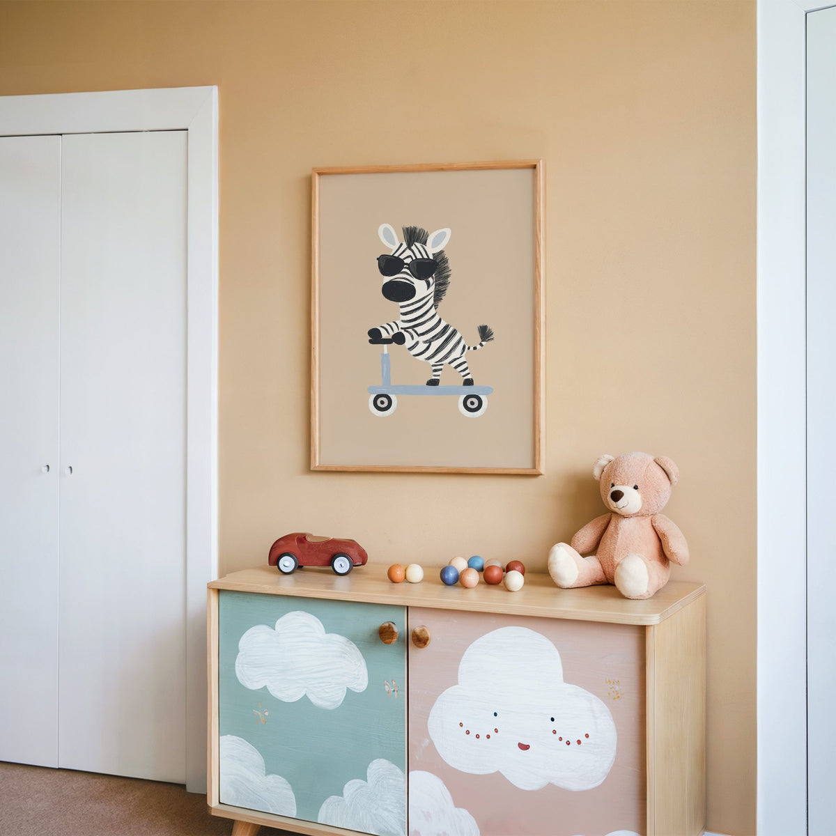 Zebra in sunglasses on scooter nursery print in an oak frame on a peach wall above a cloud-painted cabinet