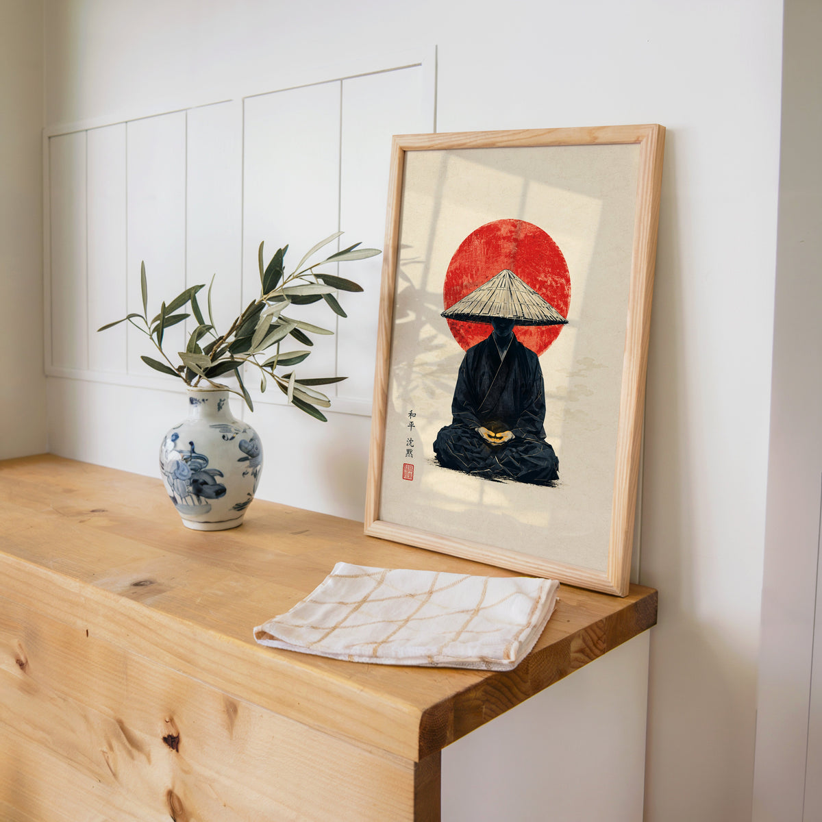 meditating monk in straw hat with red sun print in a pine frame on a wooden counter beside a blue and white porcelain vase